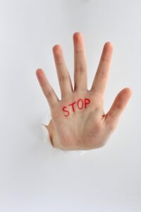 Hand with text stop written on the palm showing stop gesture through a hole in paper.