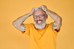 Happy funny older bearded hipster man wearing glasses isolated on yellow.