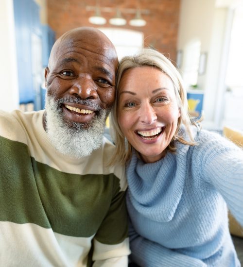 Happy senior diverse couple in living room sitting on sofa, making video call